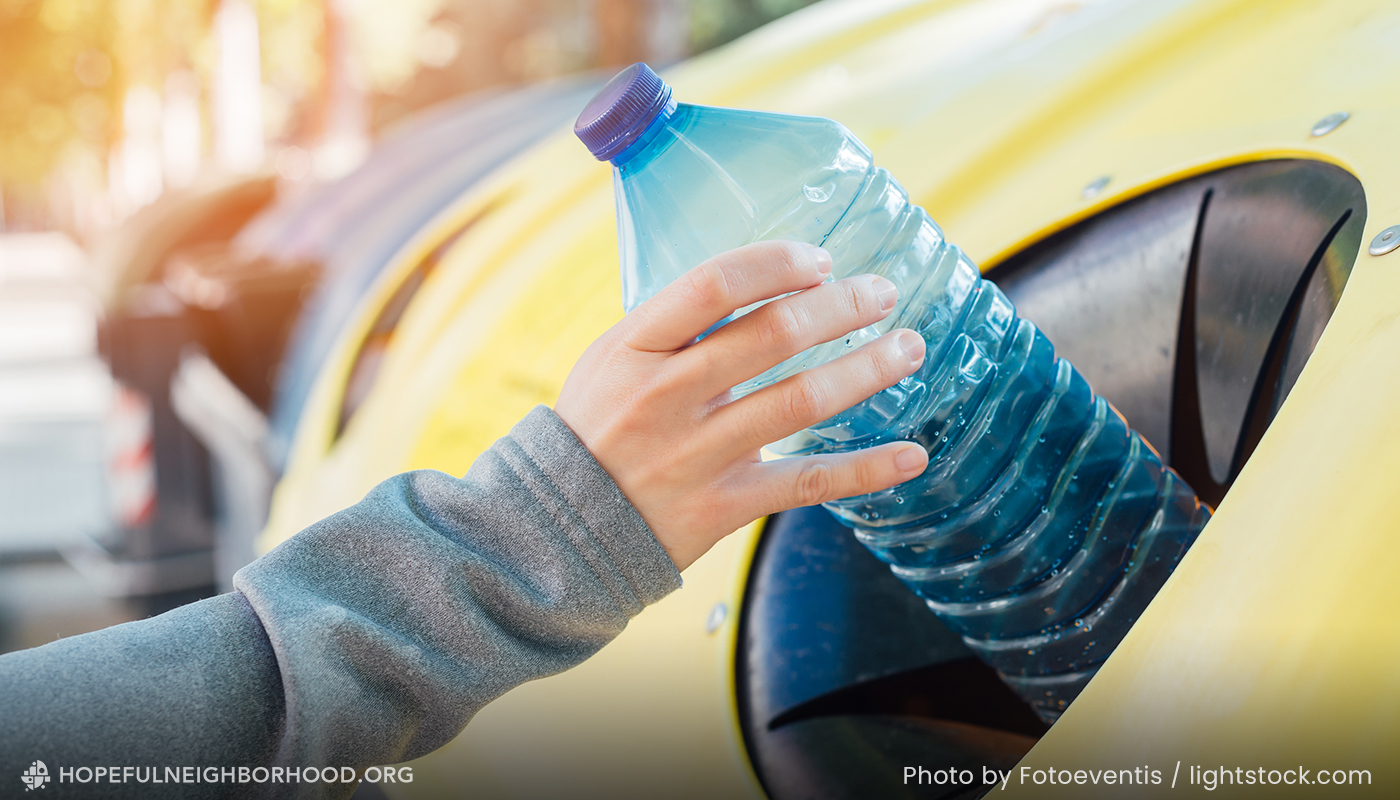 Photo showing a hand throwing an empty plastic bottle in a recycling bin.