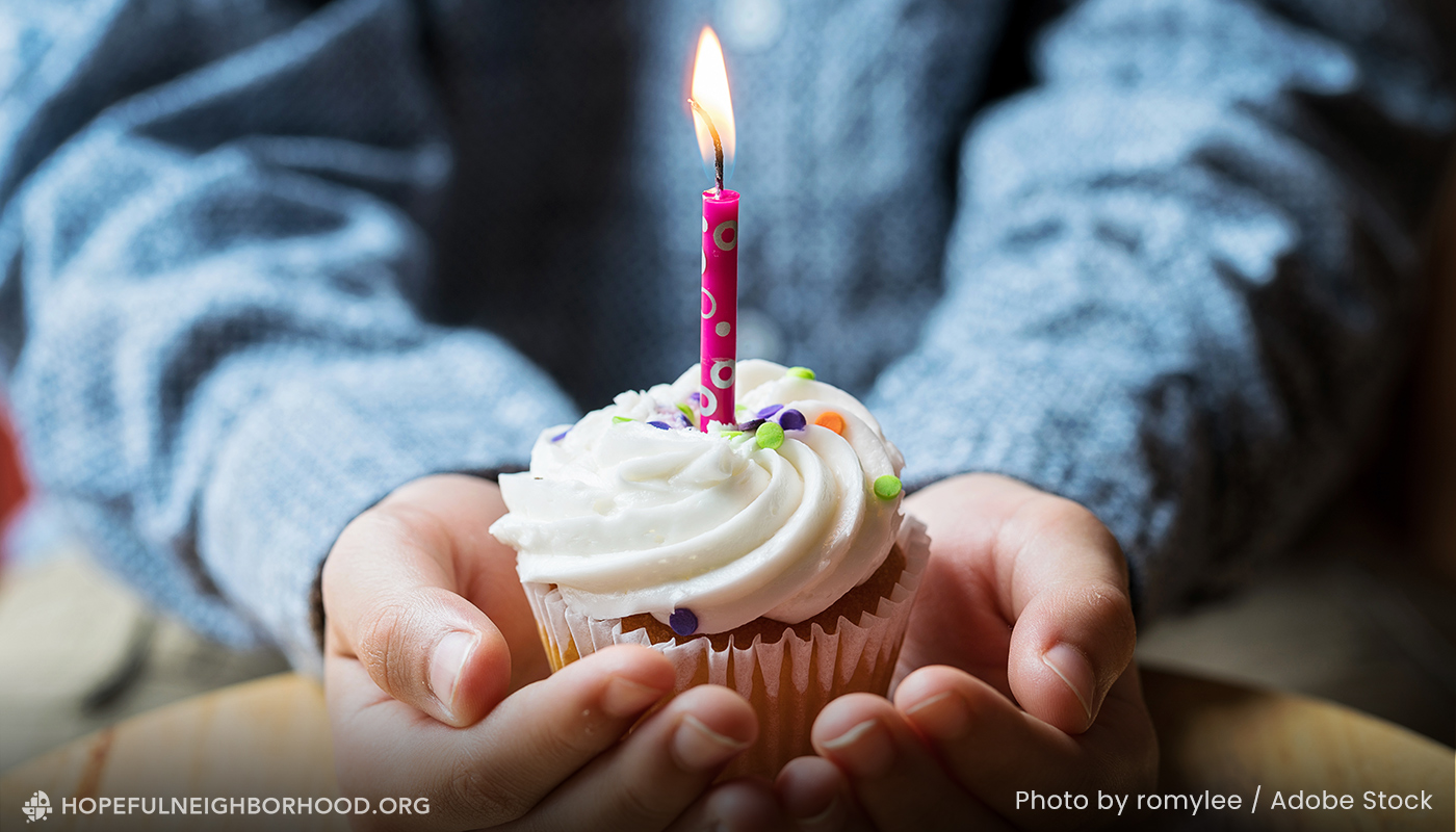 Photo of two hands holding a cupcake with white frosting and a pink birthday candle.
