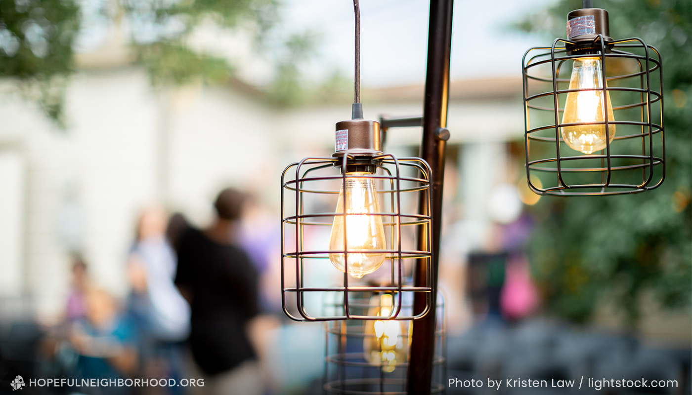 A close-up image of patio string lights with a small gathering of neighbors in the background.