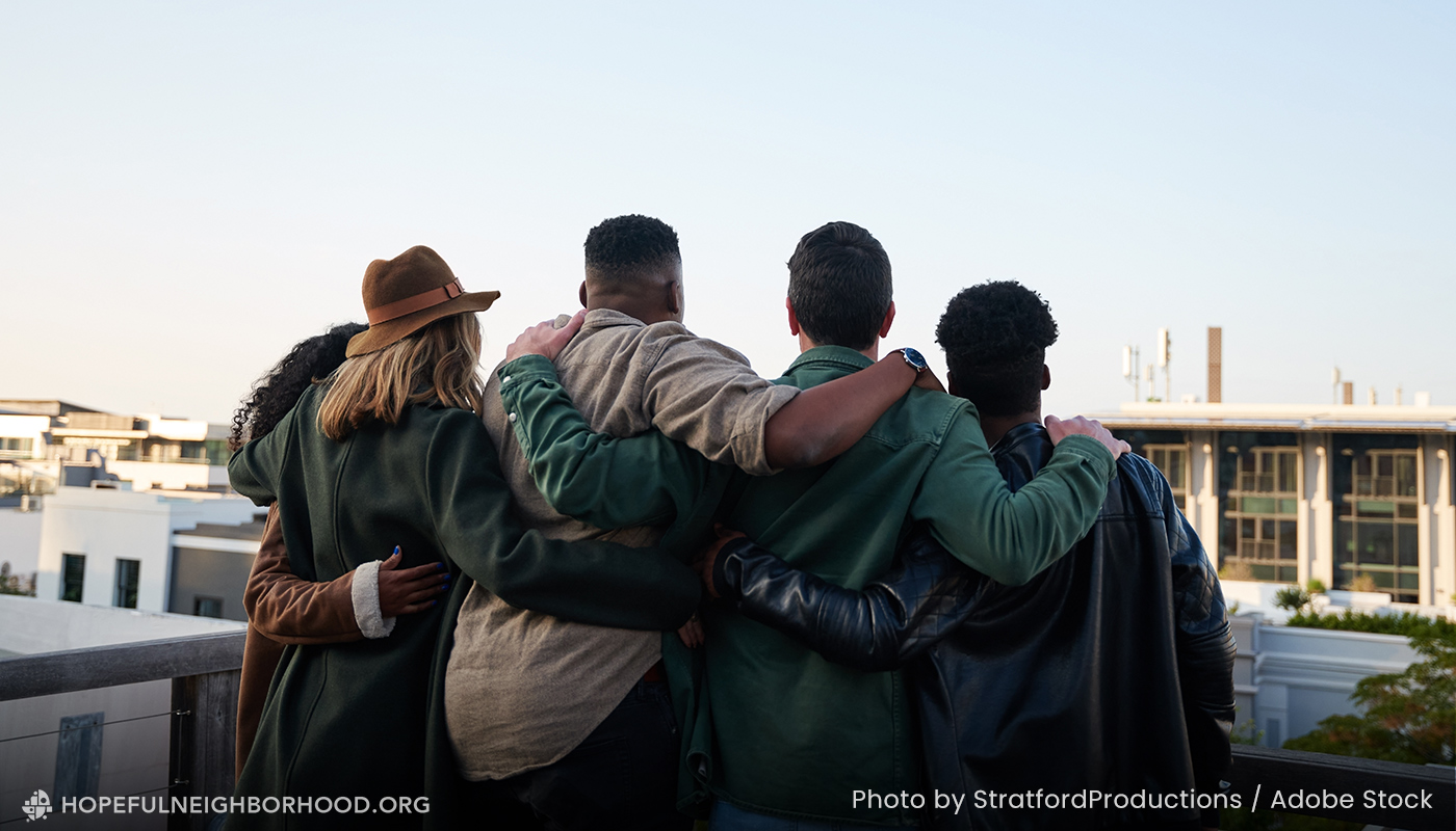 Four young adults have their arms around each other and look out over the city.