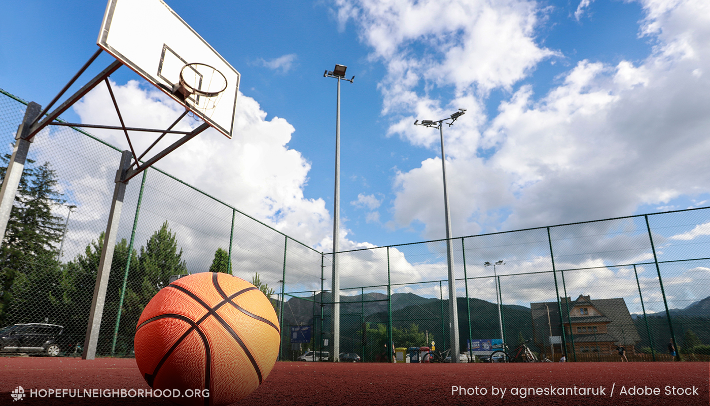 Photo of a basketball on the court with a clear blue sky and clouds behind.