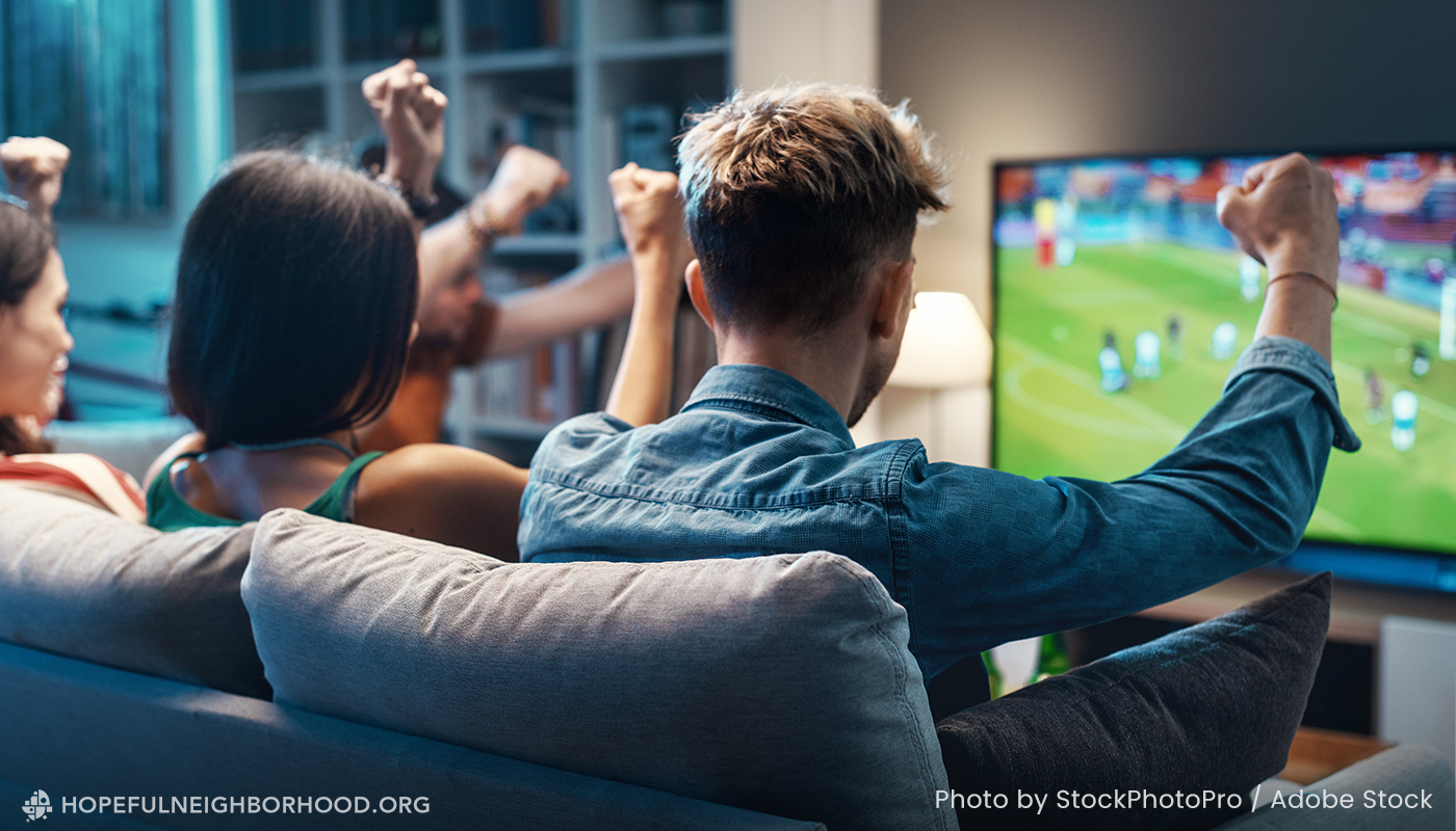 A group of friends on a couch watching a soccer game and cheering.