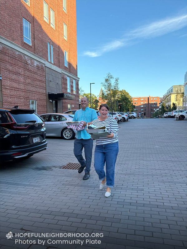 Photo shows a couple carrying dishes through a parking lot.