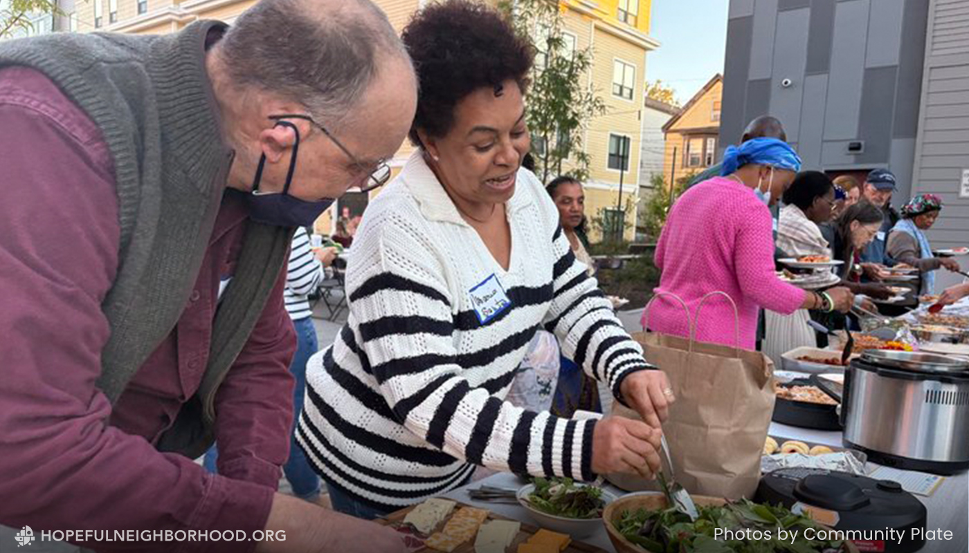 A woman is filling a bowl with salad while talking to an older gentleman at a community potluck.