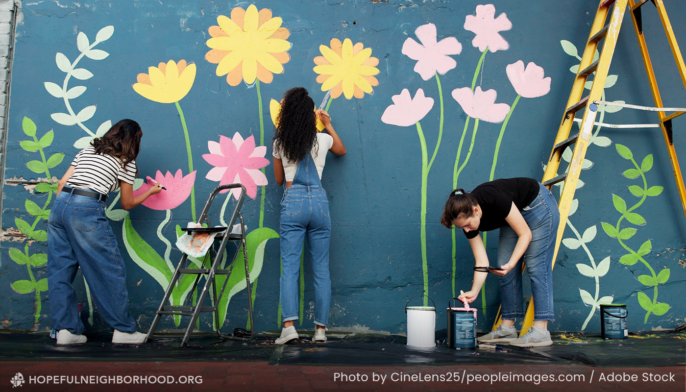 Women work together to paint a mural on a city wall.